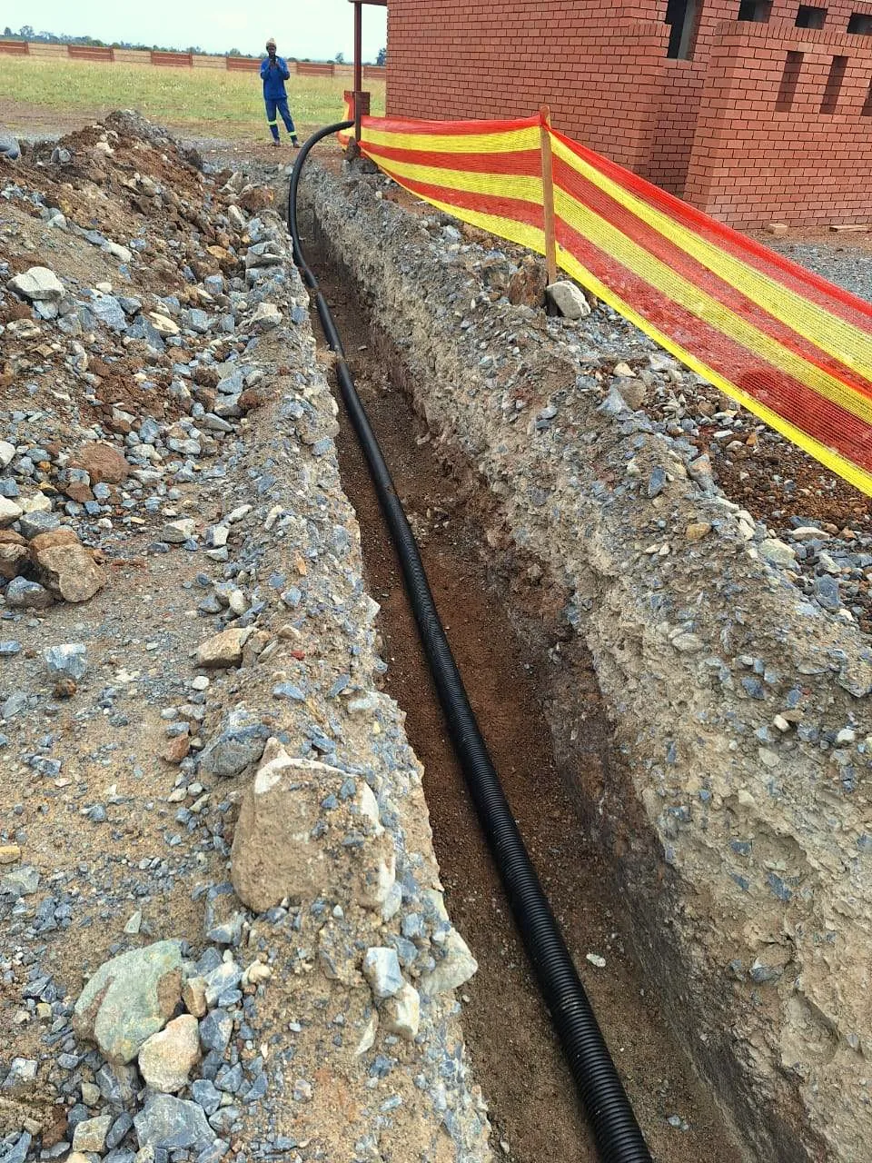 HDPE pipe laid in an excavated trench beside a new brick building